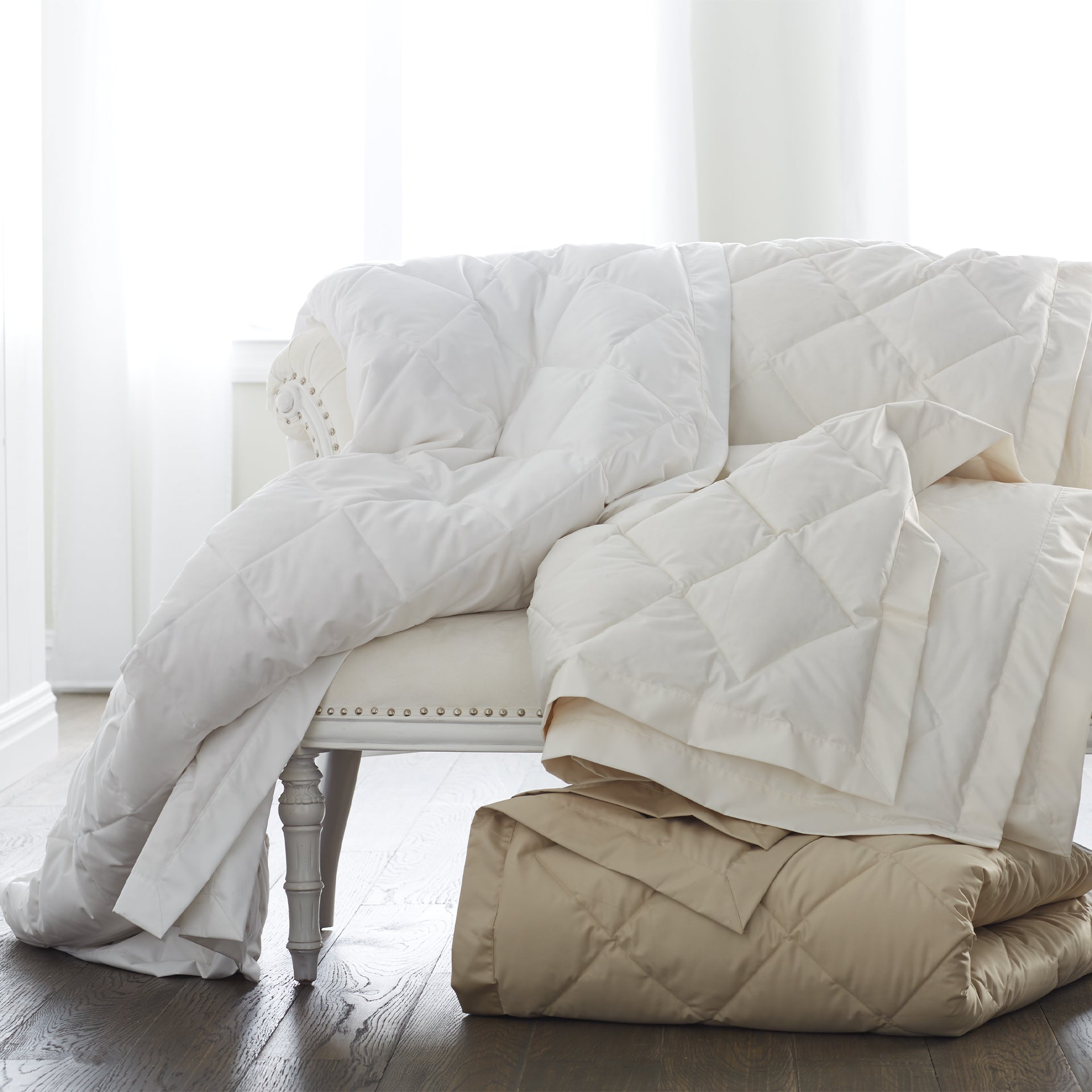 scandia home down blankets in white, ivory and café folded and draped over a sette