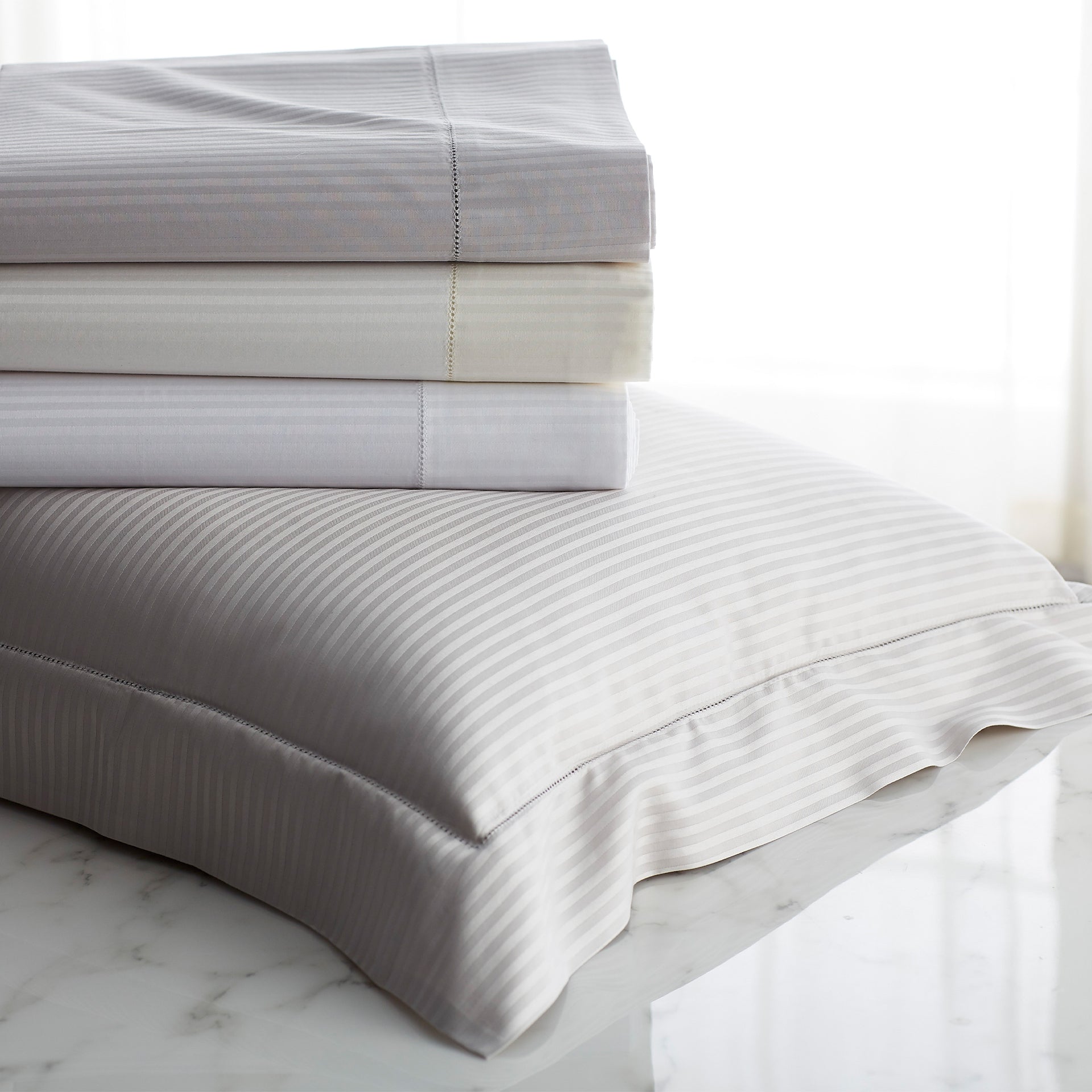 savoia stripe pillow sham shown with folded flat sheets in color ways-white, ivory and shadow