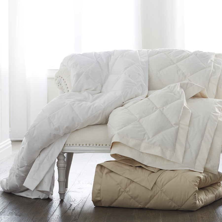 scandia home down blankets in white, ivory and café folded and draped over a sette 