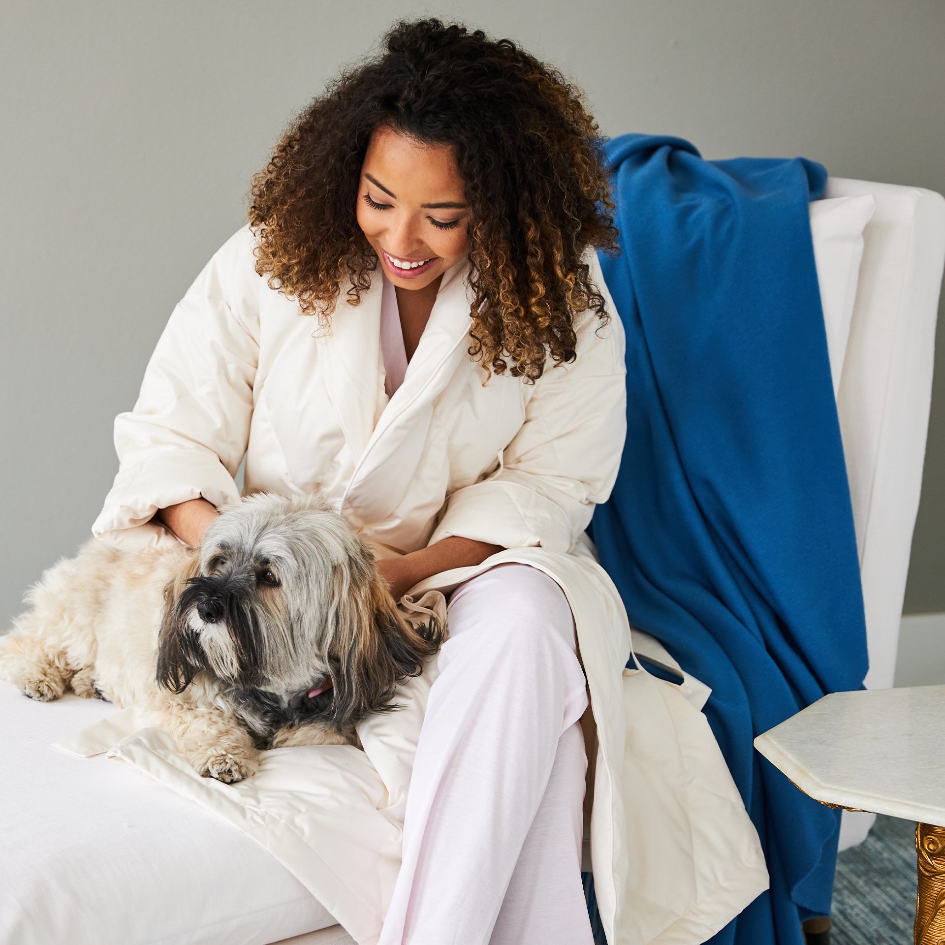 woman wearing the down robe in ivory with her dog on a chair