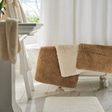 indulgence bath rugs in the colors bronze and ivory draped over bath tub