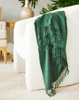 the jaya cashmere throw in the color dark green drapped around an ivory chair
