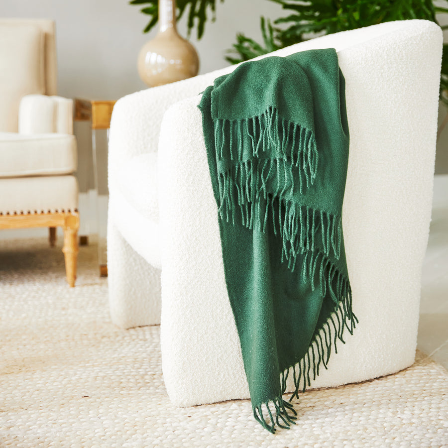 the jaya cashmere throw in the color dark green drapped around an ivory chair