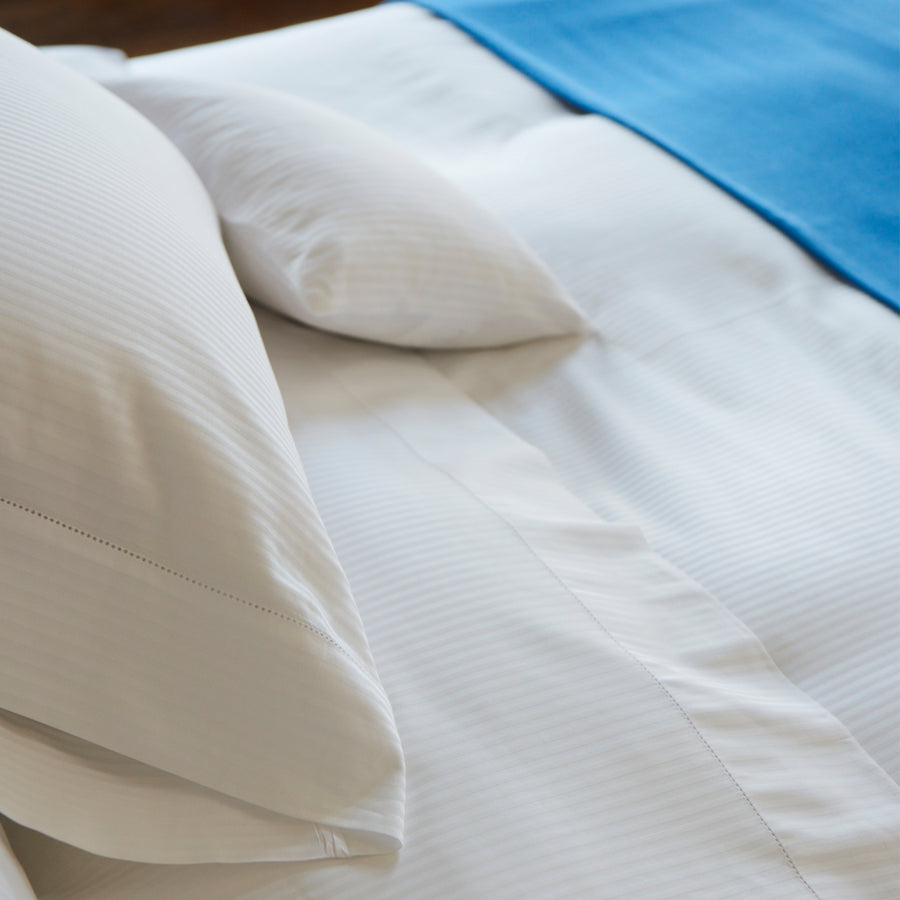 close up detail of the tone on tone striped pattern  and hemstitch finish of the savoia flat sheet shown in the color ivory
