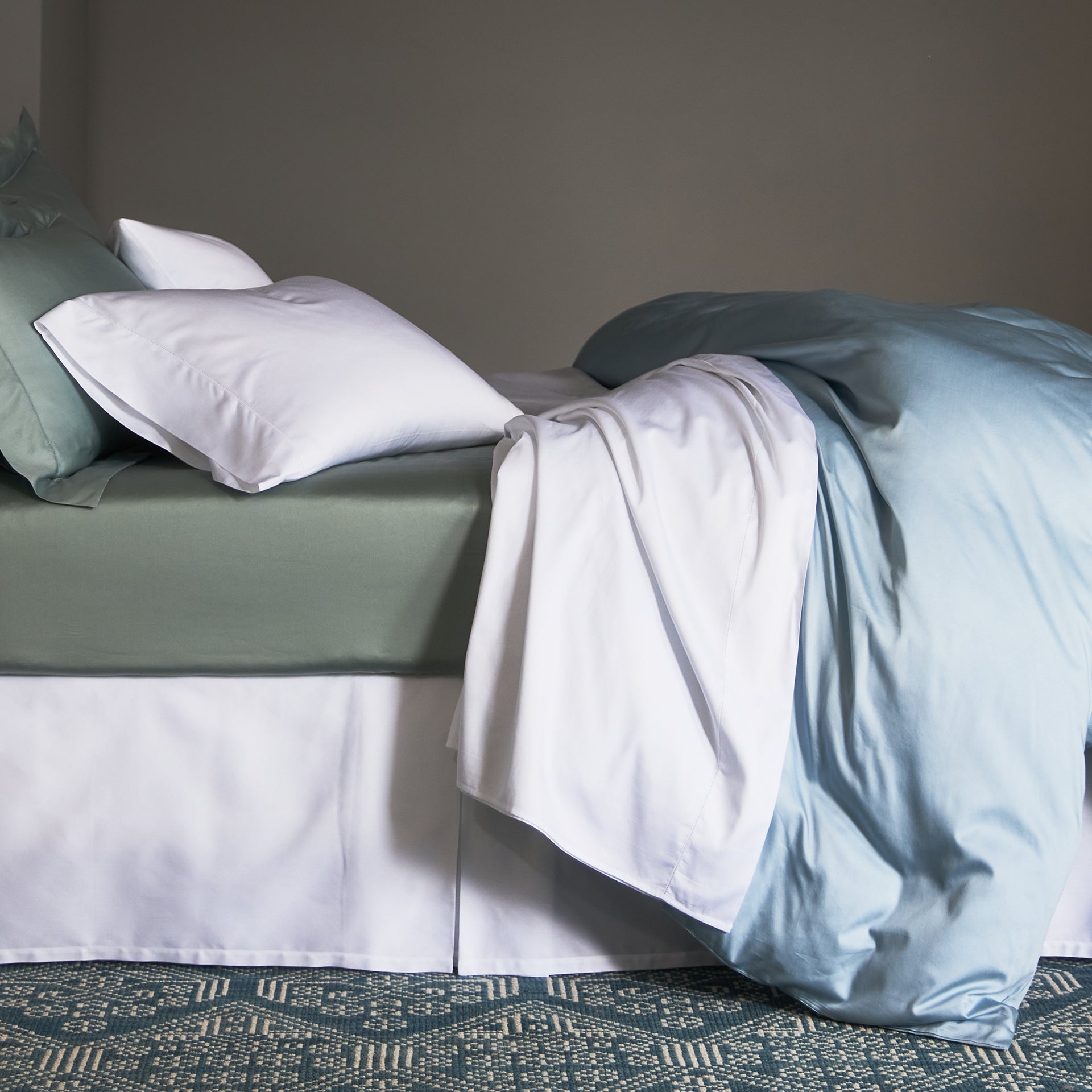 stresa flat sheet in white drapped with the stresa duvet cover in the color rain